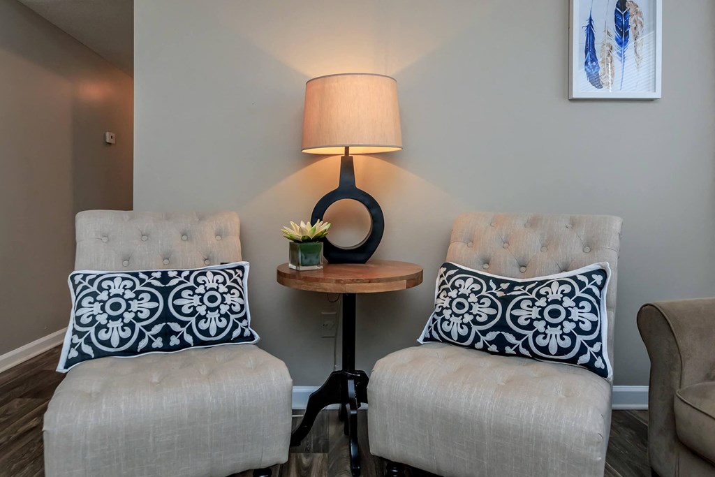 a living room with two chairs and a table with a lamp