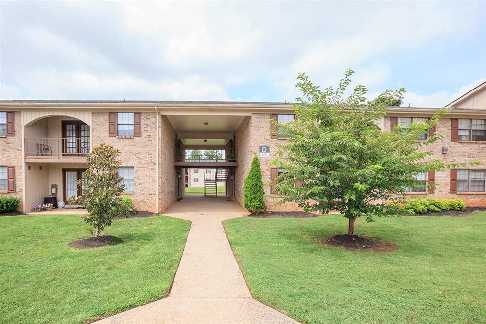 the front of a brick apartment building with a lawn and trees