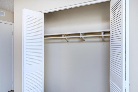 an empty closet with white shutters and a white closet door with hangers