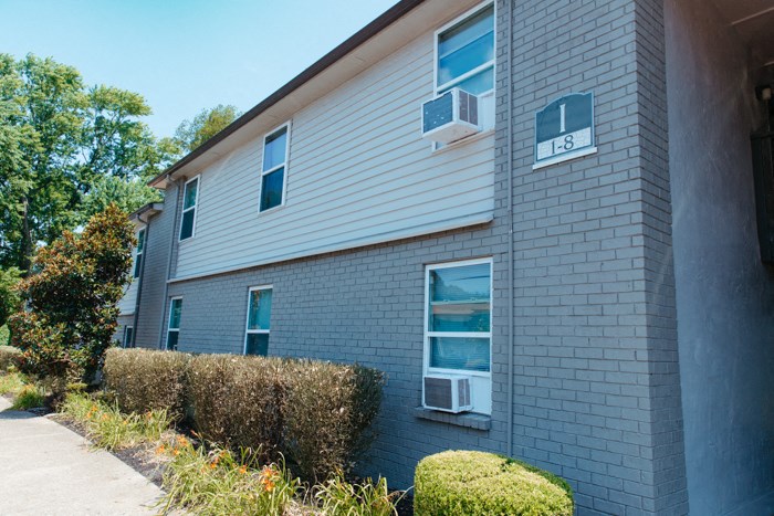 the side of a gray brick apartment building with a sidewalk