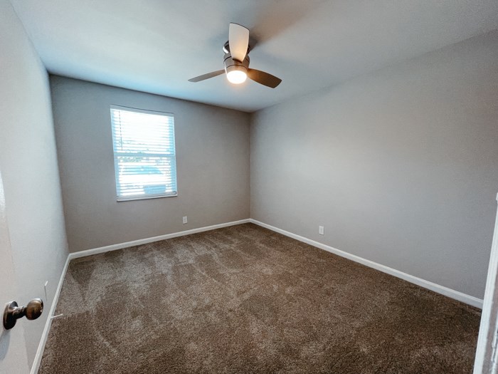an empty room with carpet and a ceiling fan