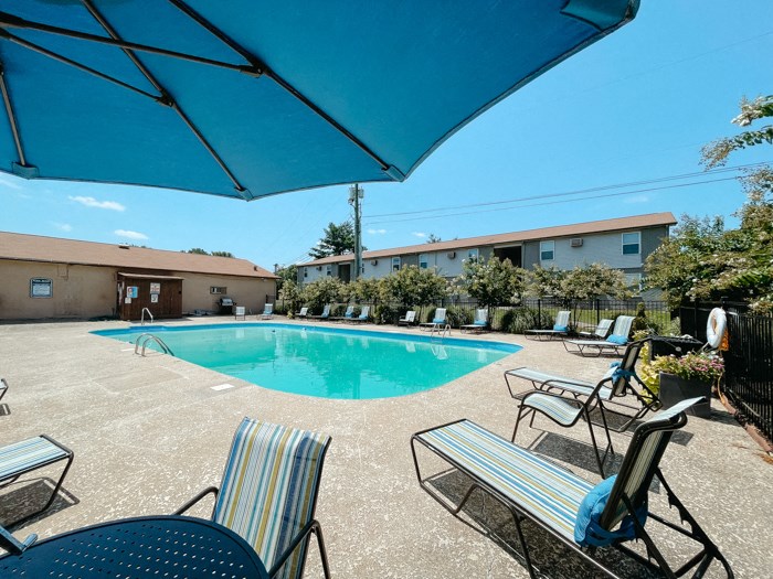 our resort style swimming pool is next to our building with chairs and a blue umbrella