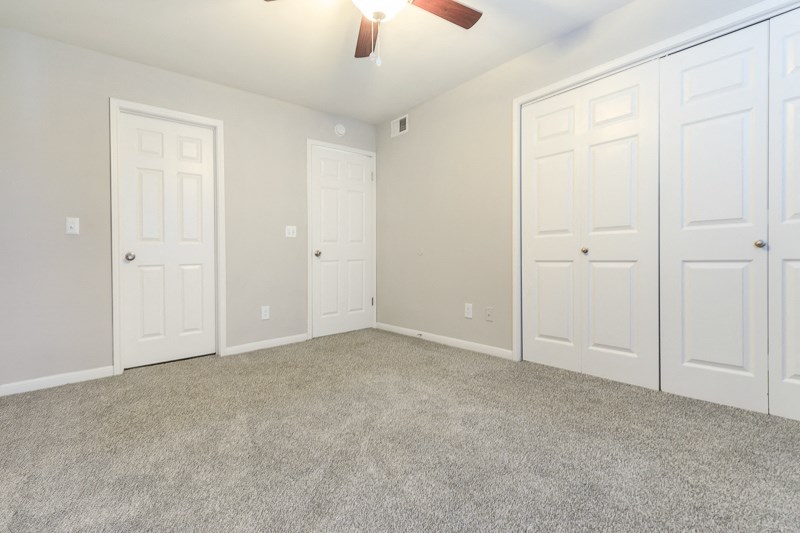 an empty bedroom with three doors and a ceiling fan