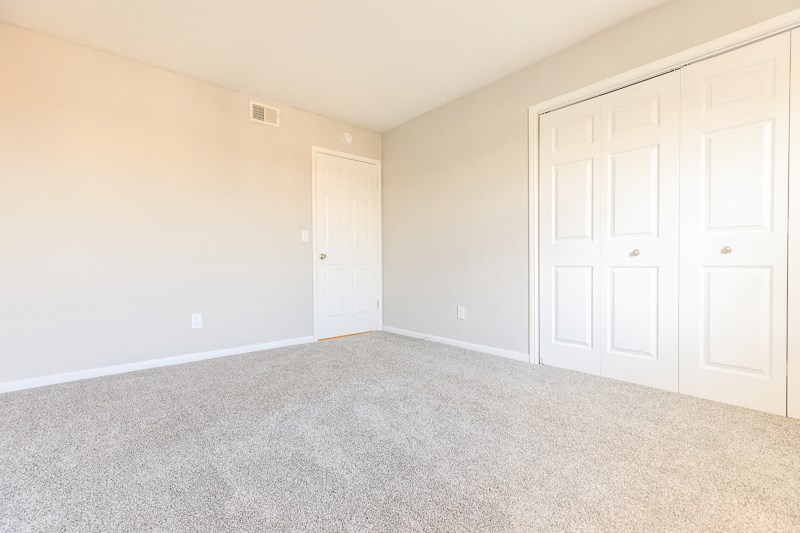 an empty bedroom with white doors and a carpeted floor
