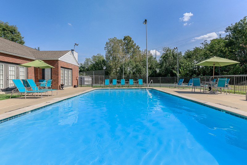 a swimming pool with blue chairs and umbrellas next to a brick building