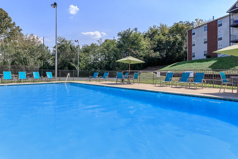 a swimming pool with blue chairs and umbrellas next to a building