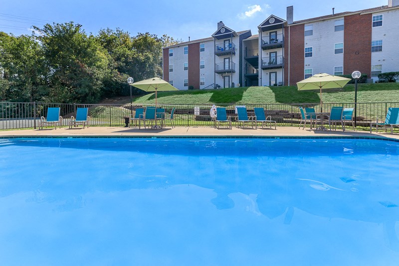 a large pool with blue chairs and umbrellas in front of an apartment building