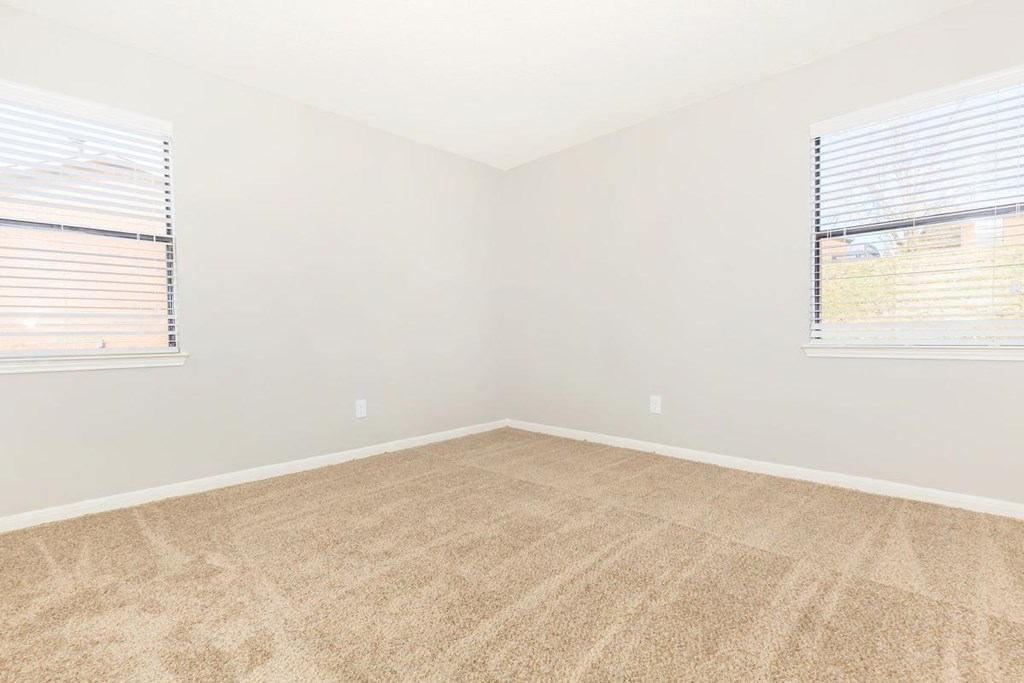an empty room with carpet and two windows