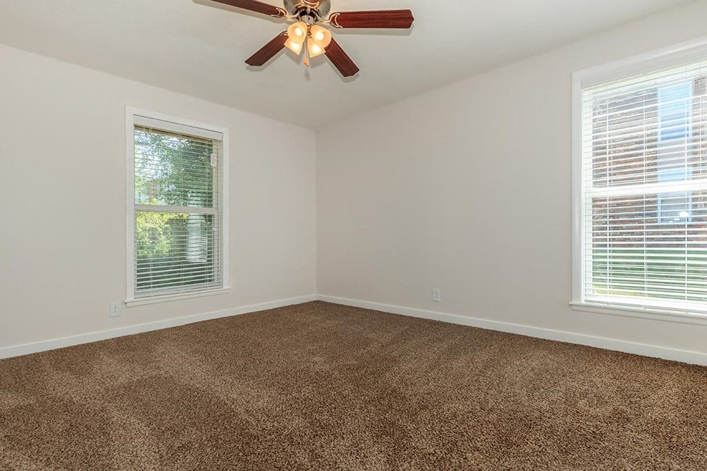 an empty bedroom with a ceiling fan and two windows