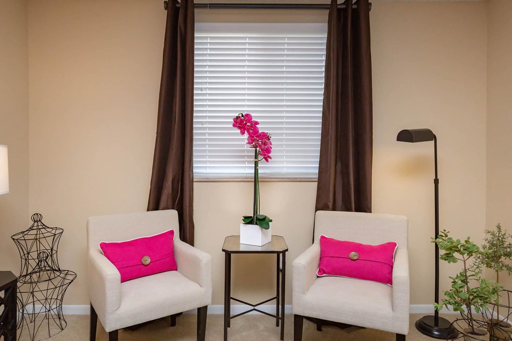 two white chairs with pink pillows sitting next to a window