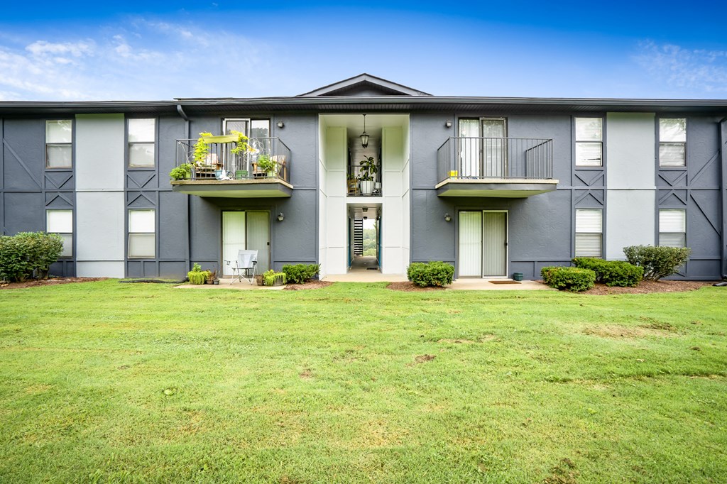 the front of a gray apartment building with a green yard
