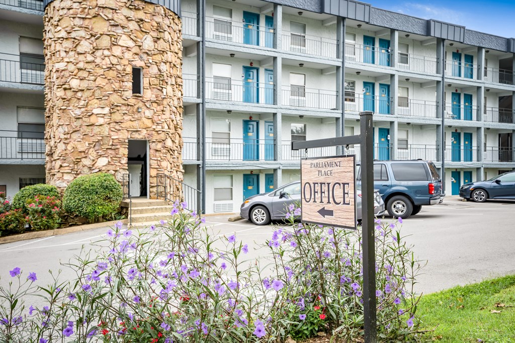 a sign in front of an apartment building with flowers in front
