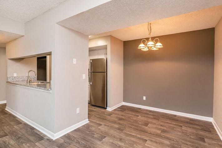 an empty living room with a kitchen and a refrigerator
