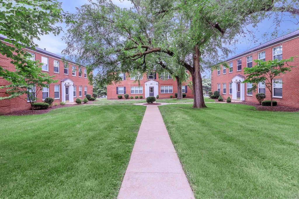 a sidewalk leading to a brick building with grass and trees