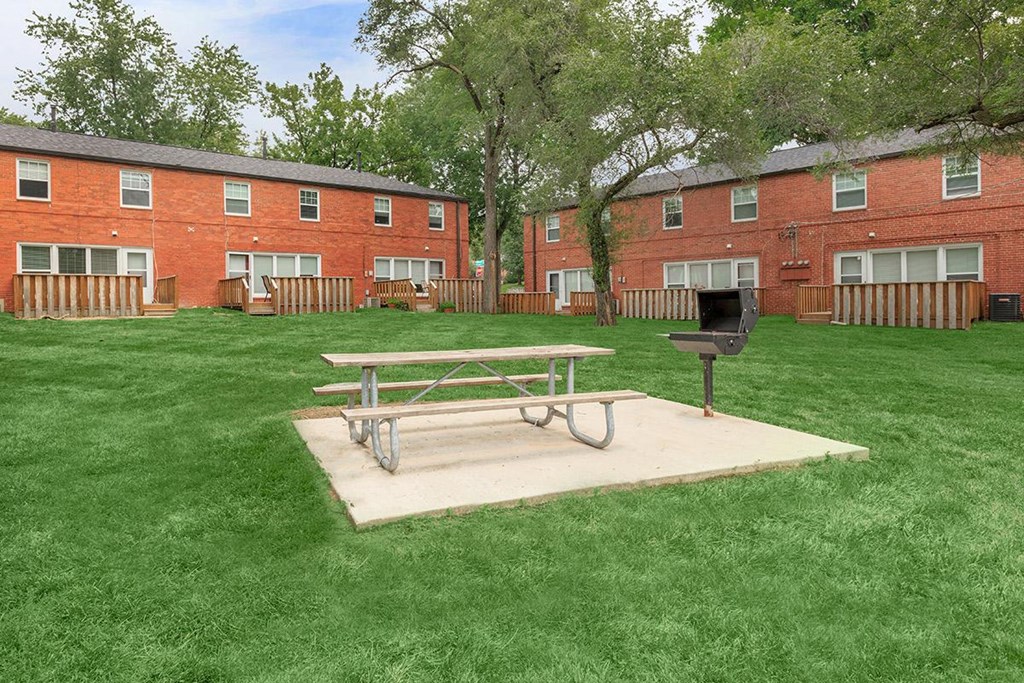 a picnic table and grill in a yard in front of a brick building