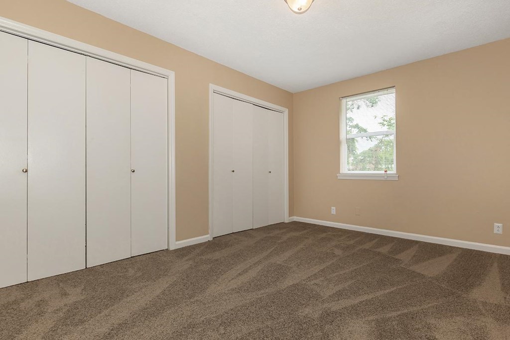 an empty bedroom with three closets and a window