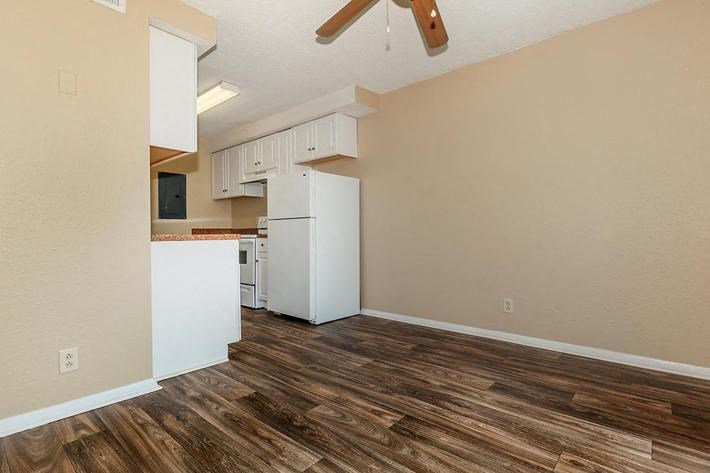an empty living room with a kitchen and a ceiling fan