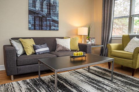 A living room with a grey couch, a coffee table, a yellow chair, and a large painting on the wall.
