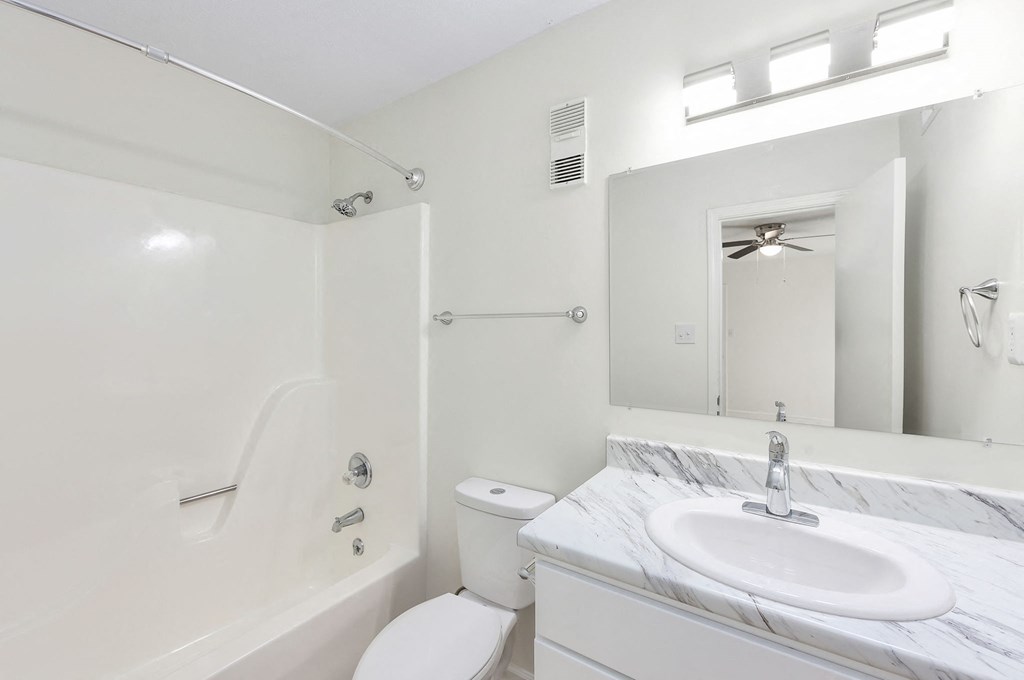 A white bathroom with a marble sink and a white toilet.