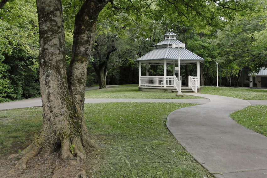 a gazebo in a park with trees and a sidewalk