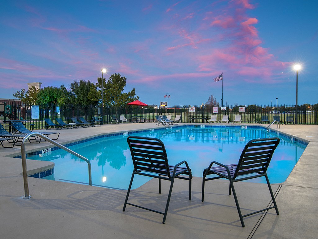a swimming pool at dusk with two chairs and chairs around it