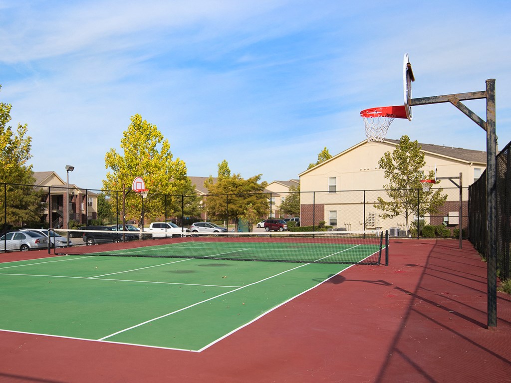 a tennis court with a basketball hoop and a building in the background