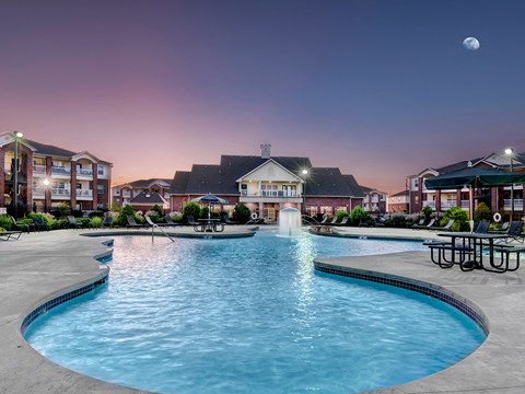 a swimming pool with a fountain at night with a building in the background