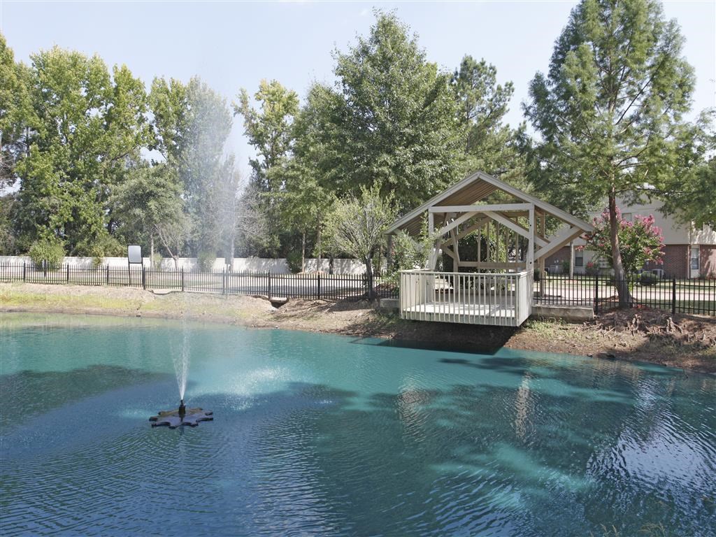 a gazebo on the shore of a pond with a fountain