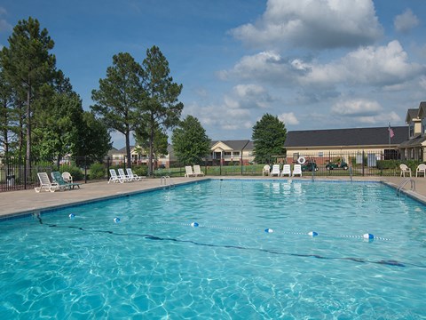 a swimming pool with chairs and trees in front of a building