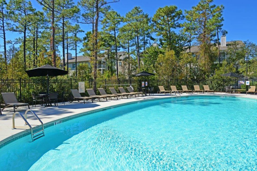 a large swimming pool with chairs and trees in the background
