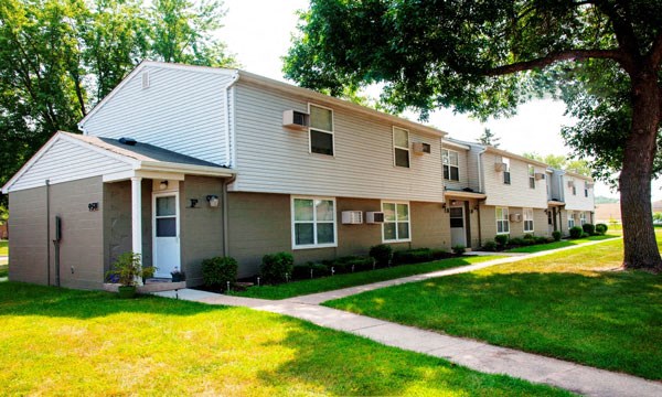 a row of apartment buildings with a sidewalk and grass