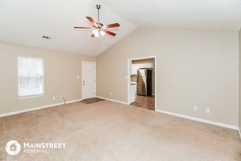 a spacious living room with beige carpet and a ceiling fan