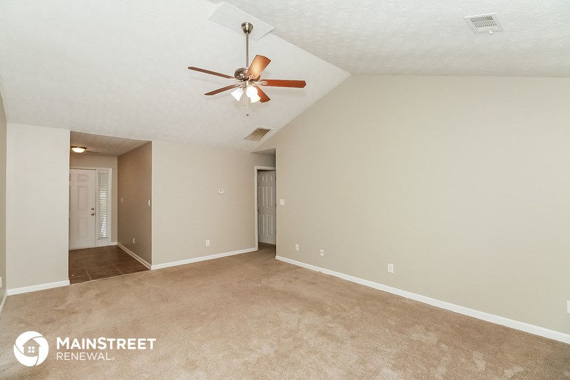 the spacious living room with ceiling fan and carpeting