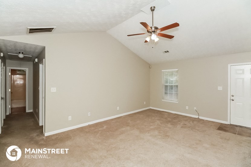 the spacious living room with ceiling fan and carpeting