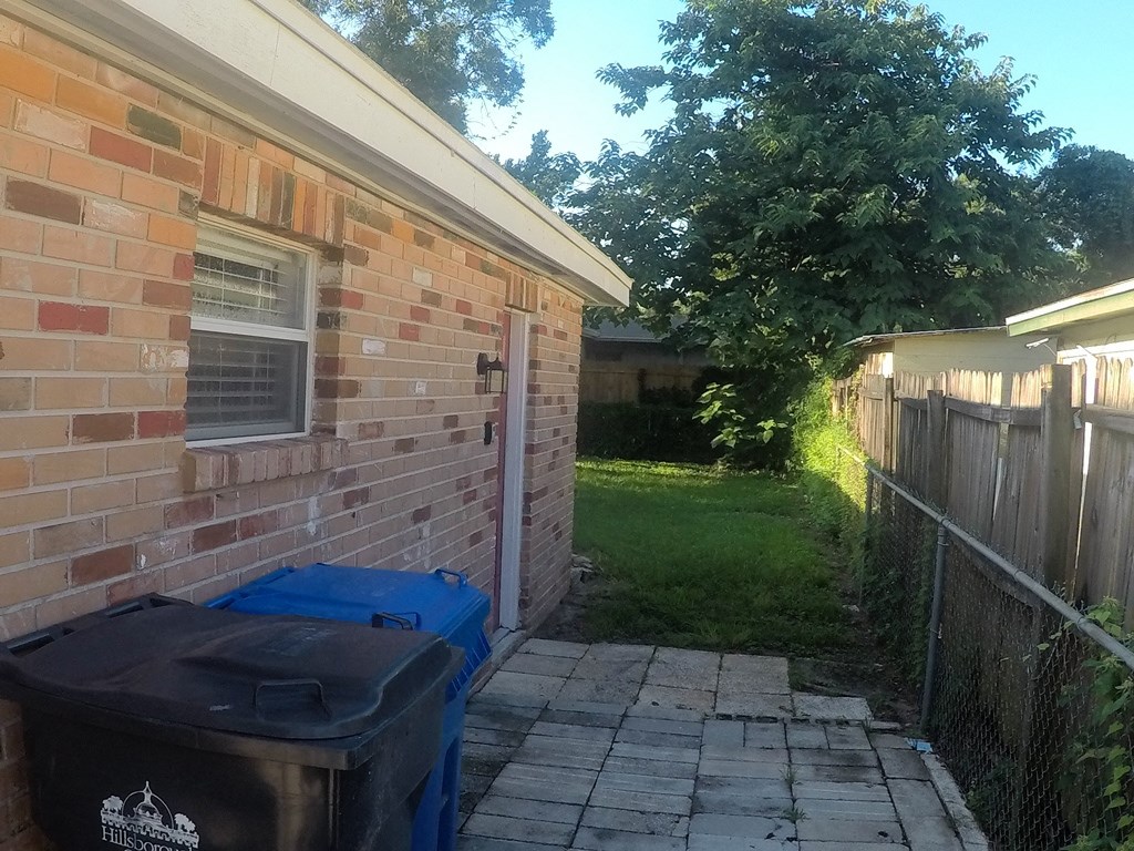 the side of a brick house with two trash cans outside