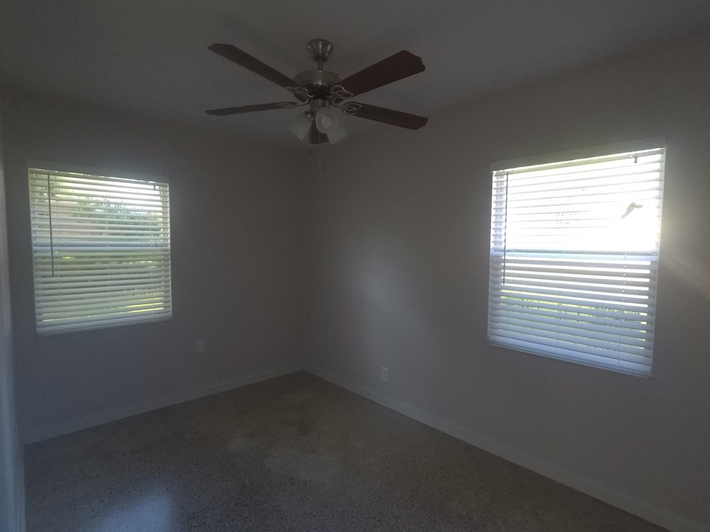 an empty room with a ceiling fan and two windows