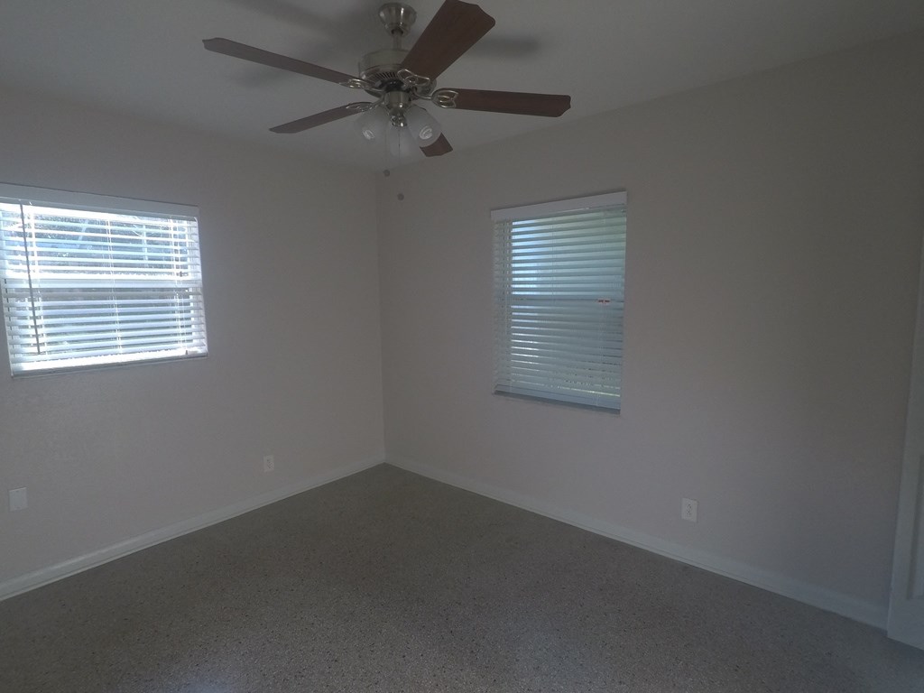 an empty room with a ceiling fan and two windows