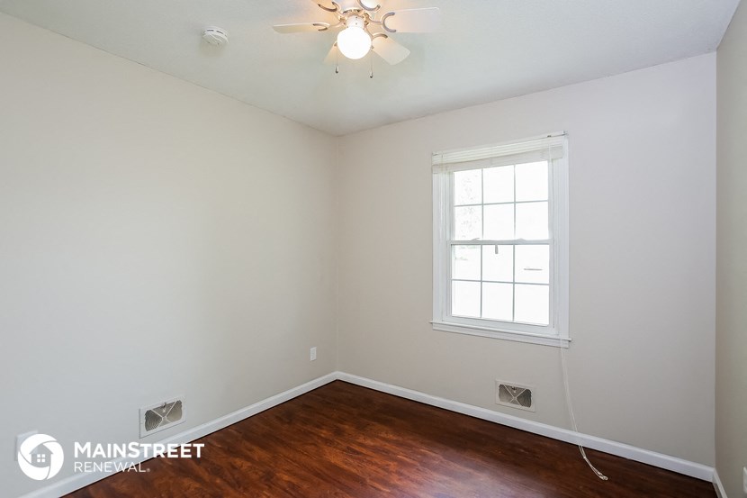 a bedroom with white walls and a window and wood floors