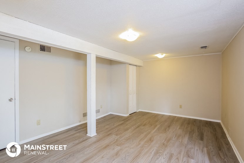 the spacious living room of an apartment with wood flooring and white walls