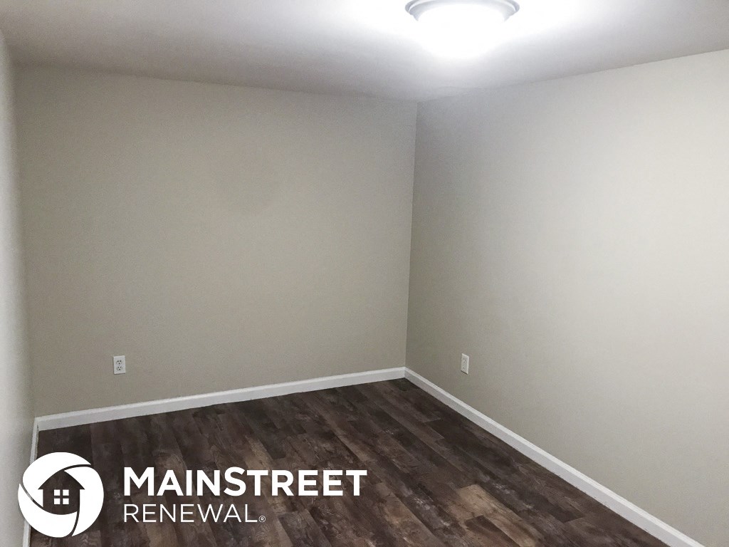 a room with white walls and wood flooring and a white lamp on the ceiling