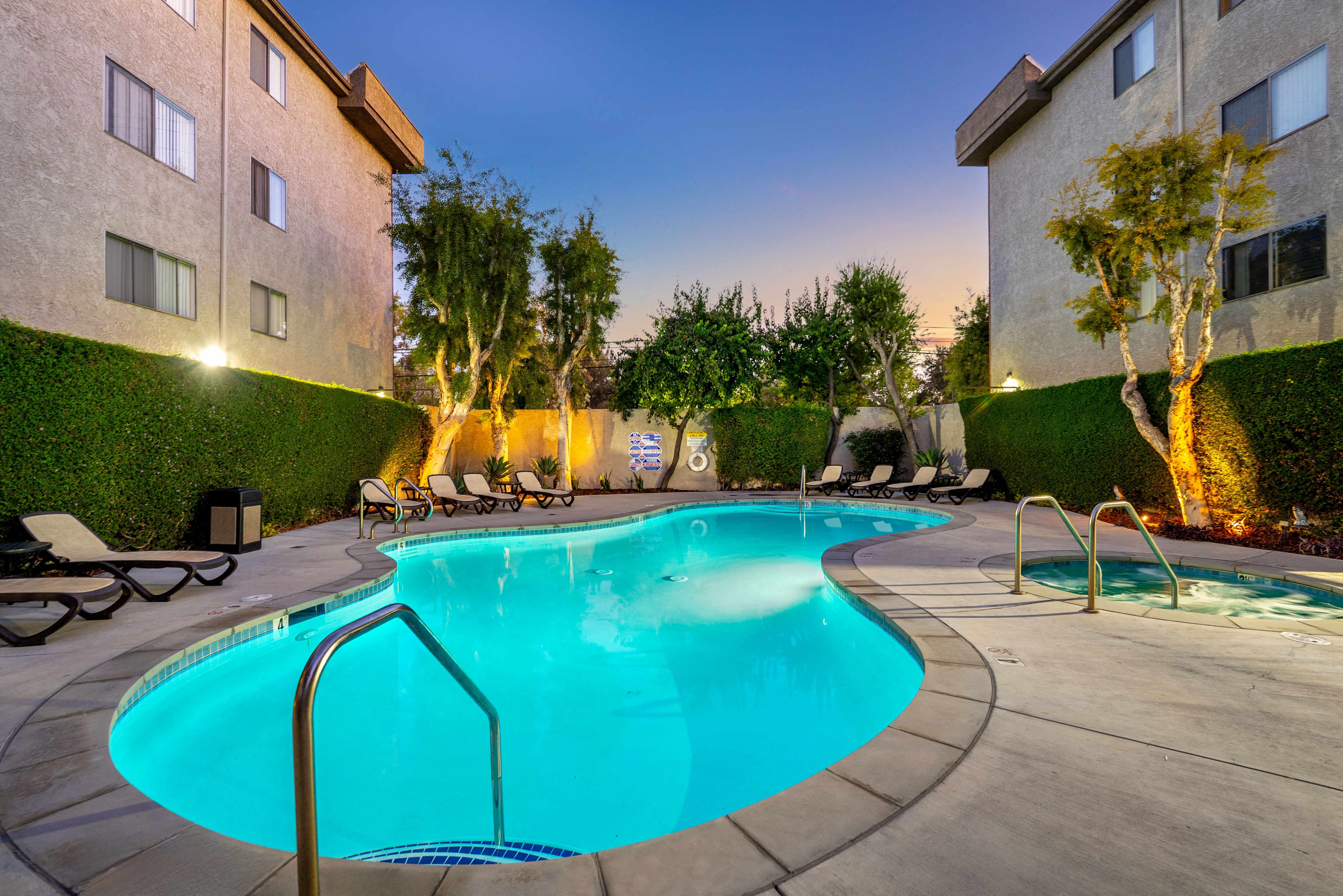 A glowing, swimming pool at the Parkview Apartments in Lake Balboa. The turquoise water is lit from within, with lounge chairs on the surrounding deck and warmly lit trees against a twilight sky.