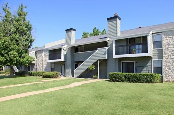 an apartment building with a green lawn and trees
