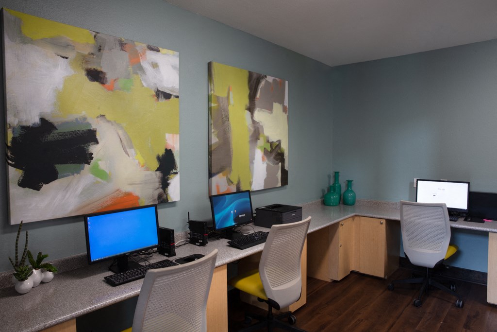 an office with three computers and two paintings on the wall