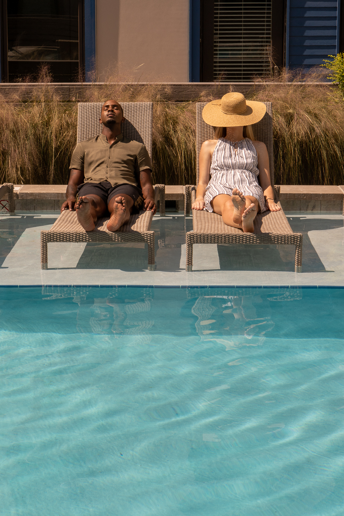 a man and woman sitting on chairs at the edge of a swimming pool
