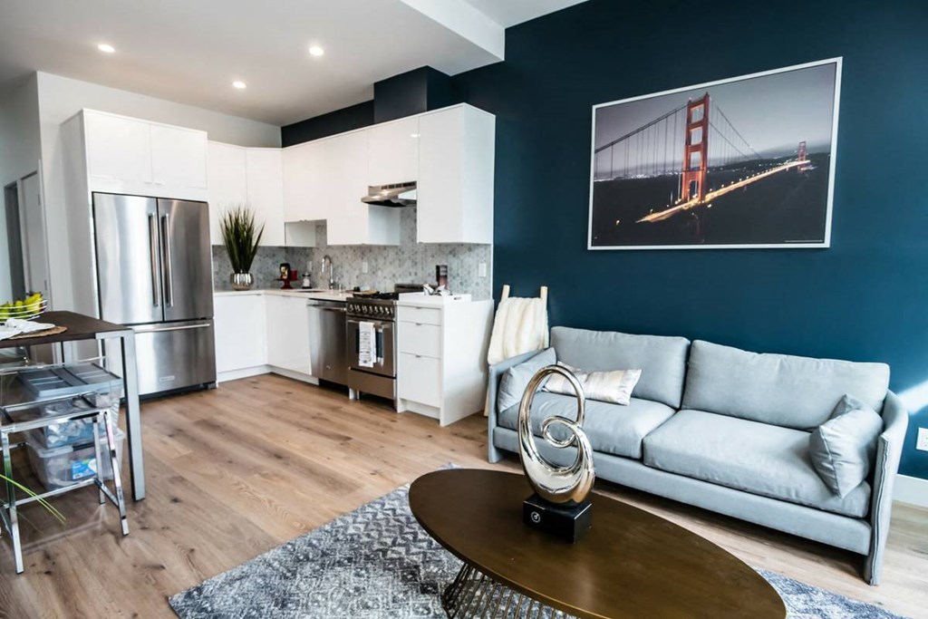 Open-concept living room with couch and coffee table and a kitchen area with upgraded appliances.