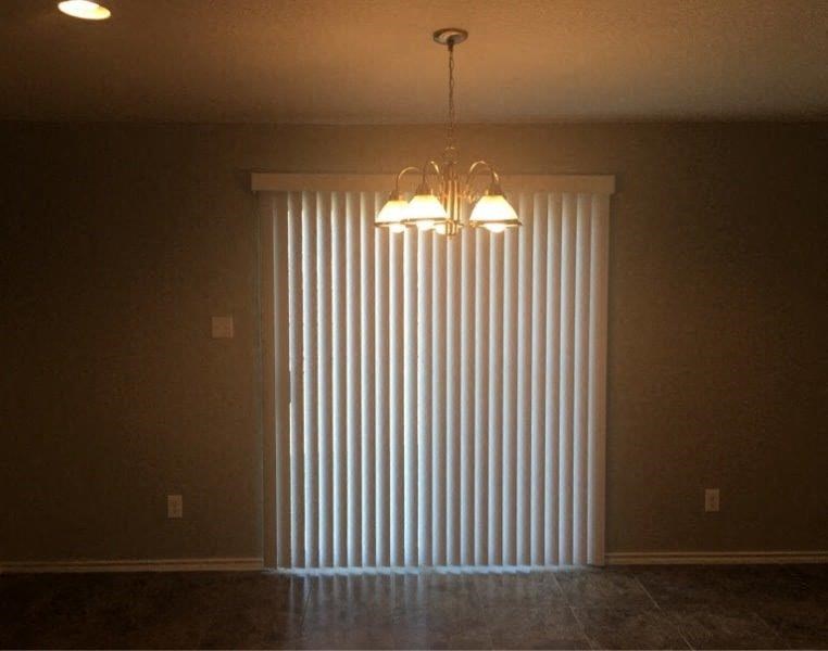 an empty living room with a large window and a chandelier