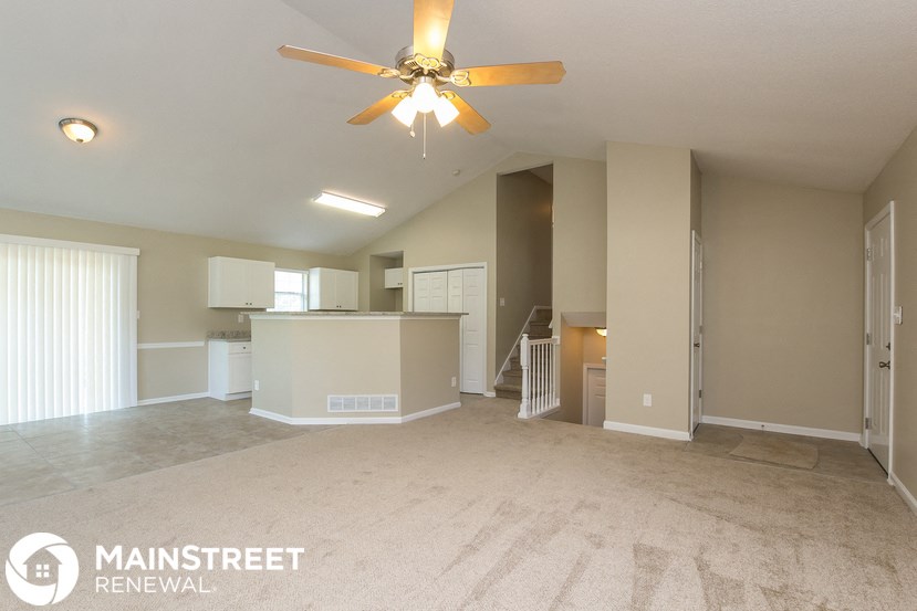 an empty living room with a ceiling fan and a kitchen