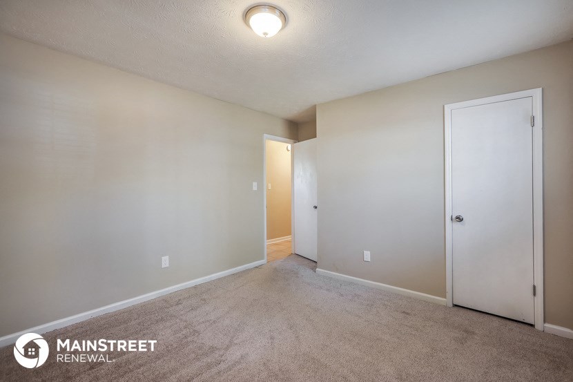 the living room of an apartment with carpet and a door to the bathroom