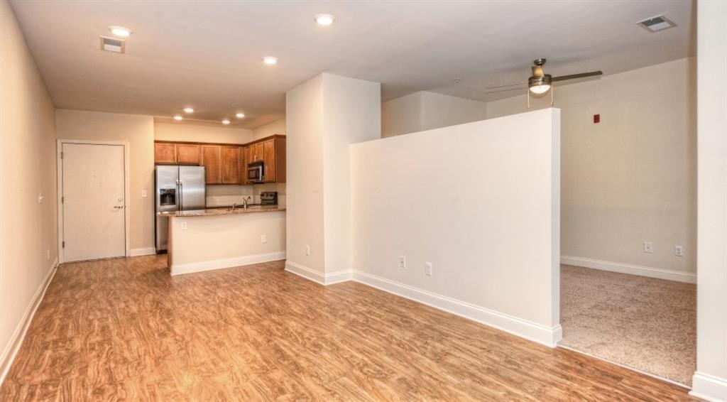 an empty living room with a kitchen in the background