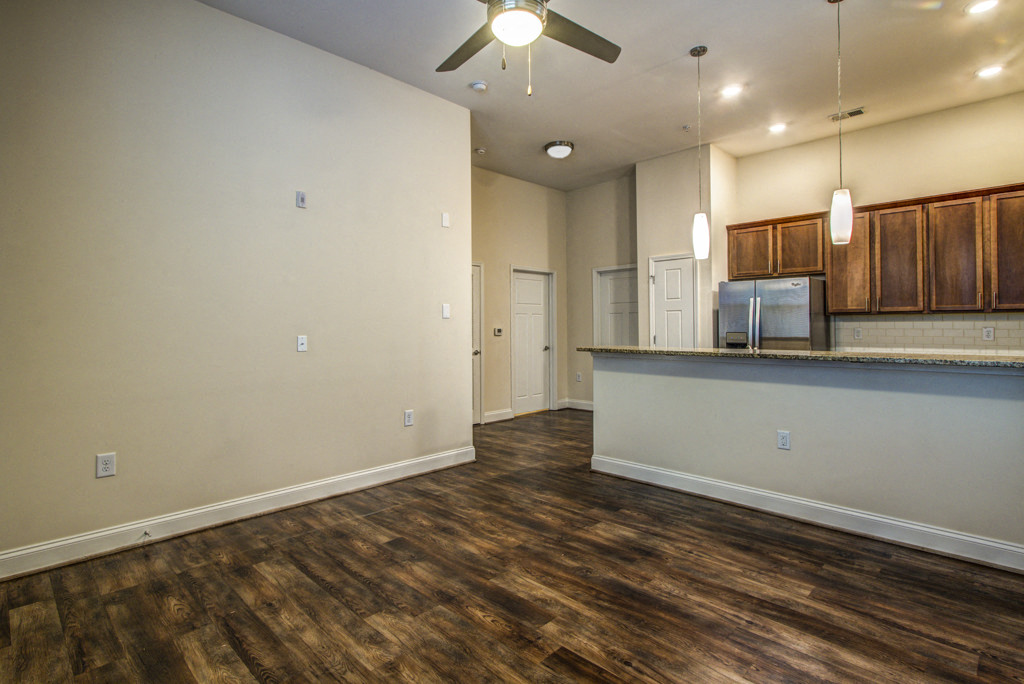an empty living room with a kitchen and a ceiling fan